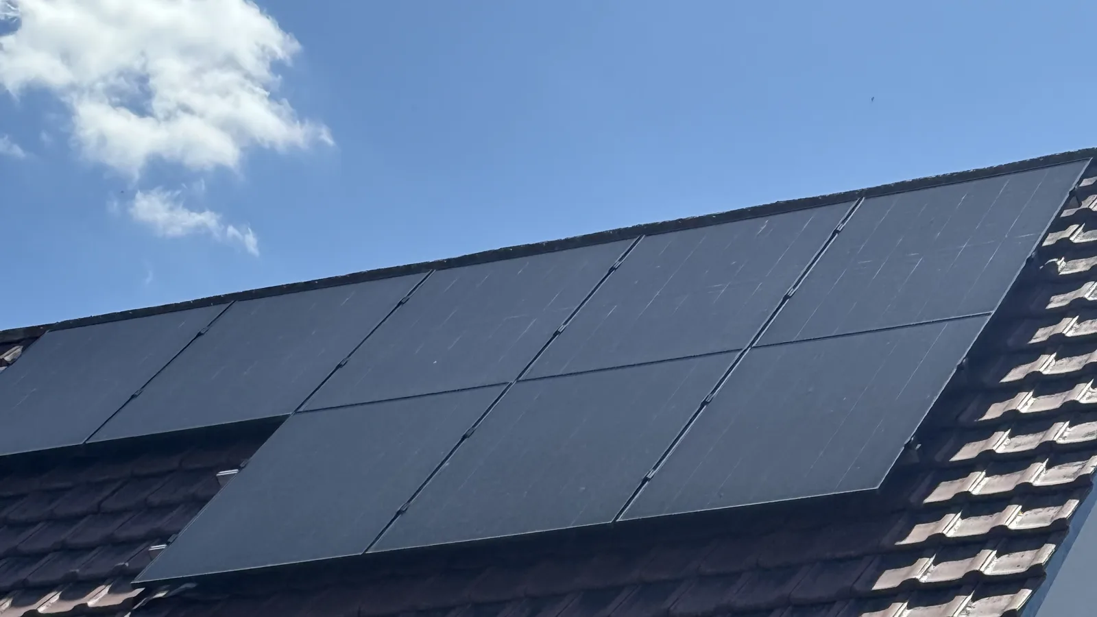 Schwarze Photovoltaik-Module auf einem Ziegeldach bei blauem Himmel